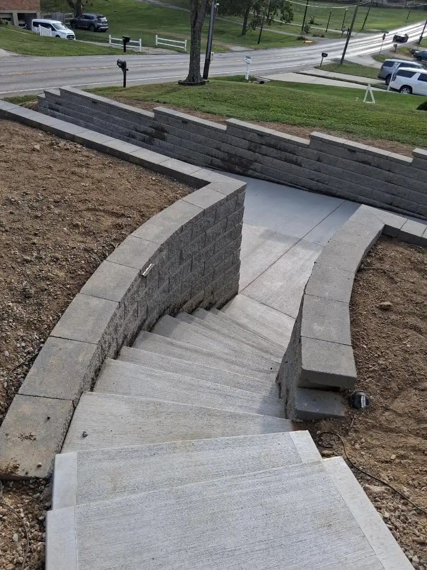 Curved capped block wall wrapping the concrete steps and walkway in Cincinnati, OH, with the lower street wall behind