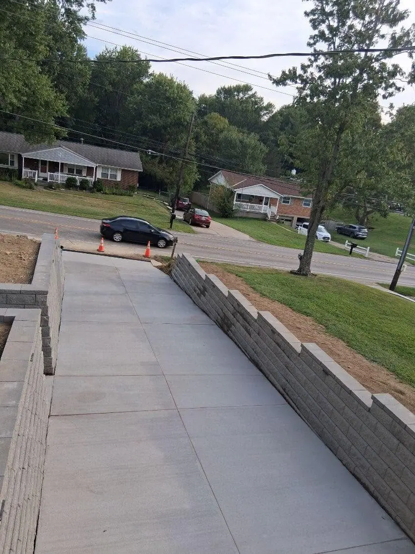 Finished concrete driveway in Cincinnati, OH falling away toward the road with the stepped block wall on the right