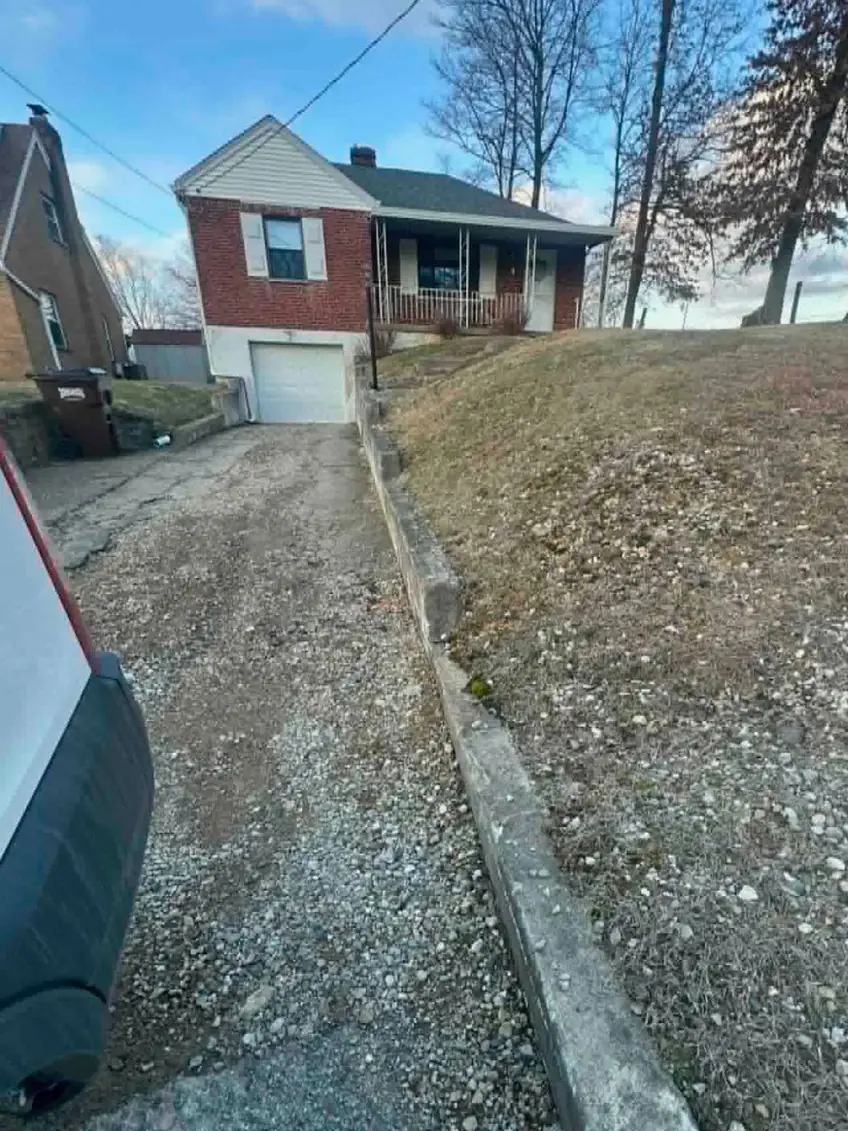Gravel and broken asphalt driveway running up to the garage in Cincinnati, OH, with the old low concrete wall along the bank