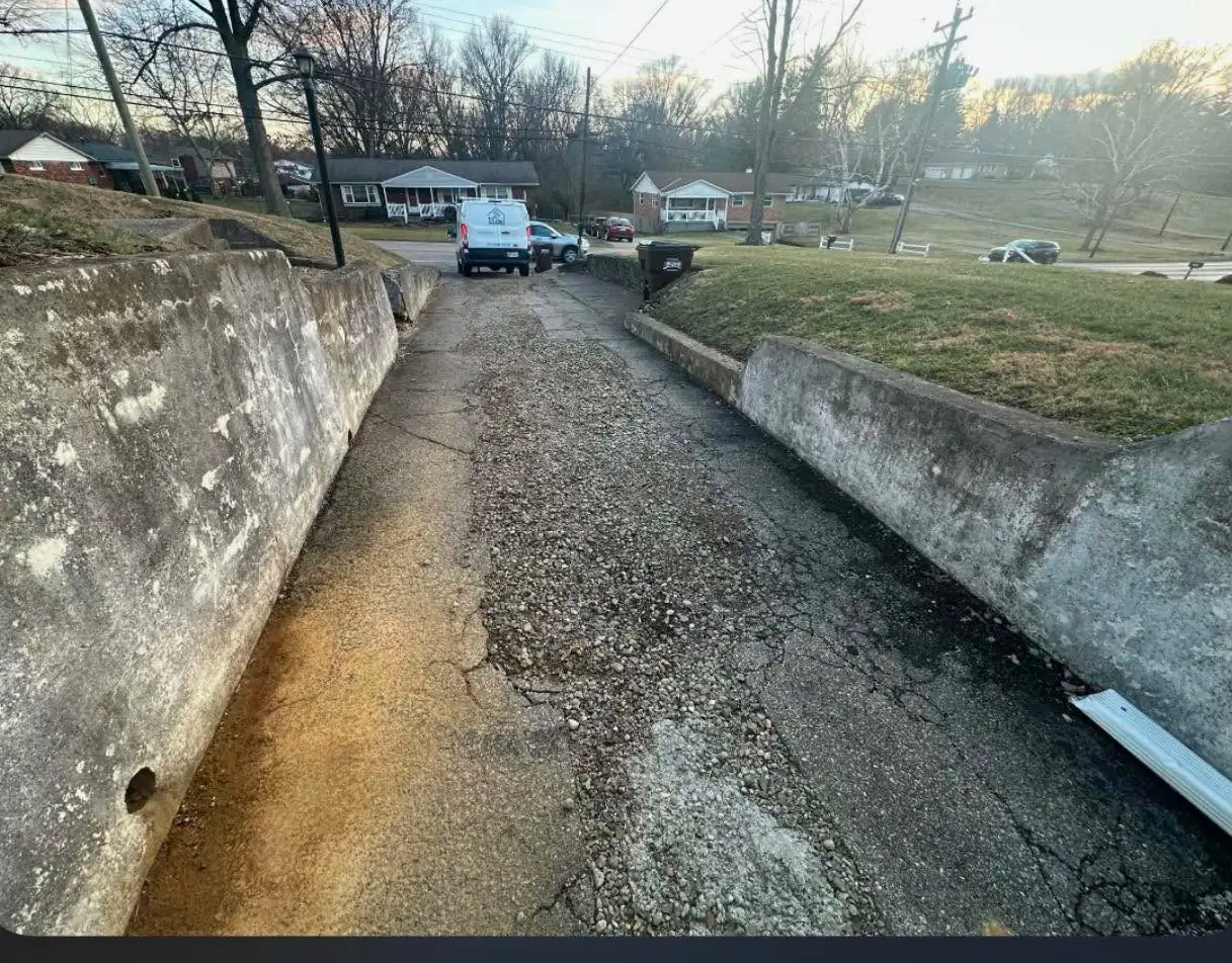 Cracked driveway between two aging concrete retaining walls in Cincinnati, OH, looking down toward the road