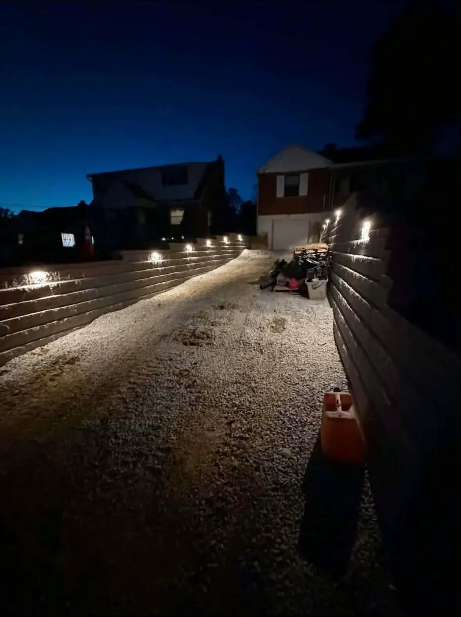 Lit block retaining walls at dusk in Cincinnati, OH looking up the gravel base toward the house and garage