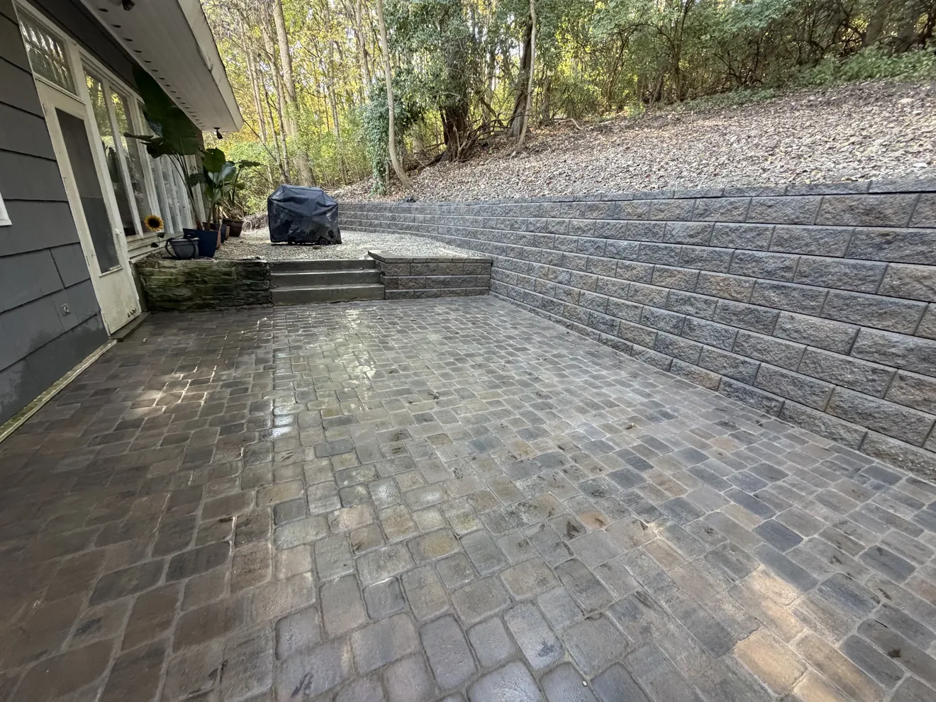 Paver patio along the back of the house in Cincinnati, OH, with a capped block retaining wall holding the hill on the right