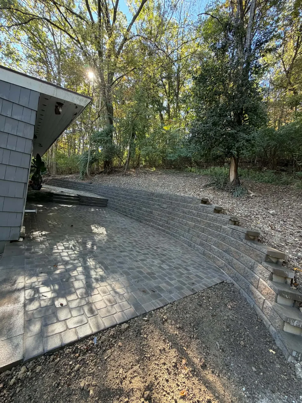 Curved block retaining wall wrapping the new paver patio in Cincinnati, OH, looking out toward the trees