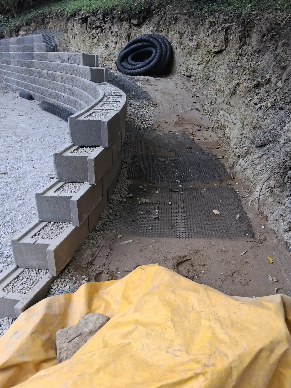 Geogrid laid back from a block course into the hill in Cincinnati, OH, with drain pipe coiled behind