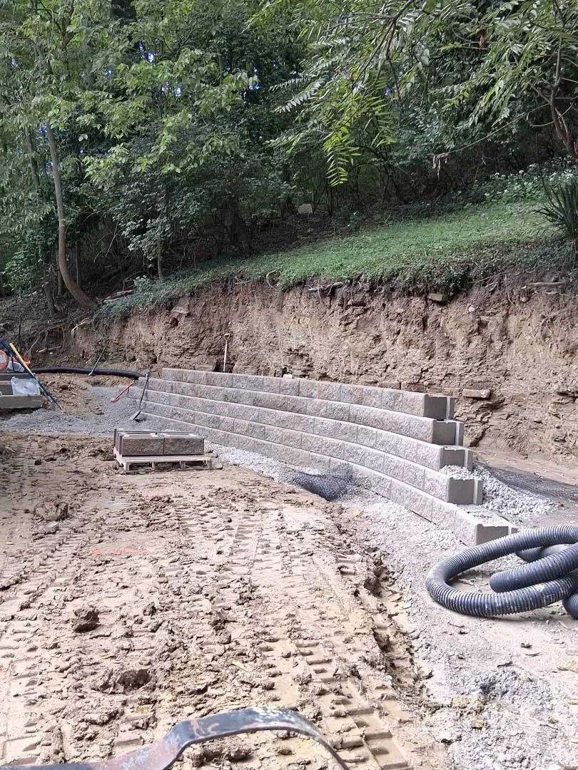 First courses of retaining wall block set against the cut hillside in Cincinnati, OH, with drain pipe ready