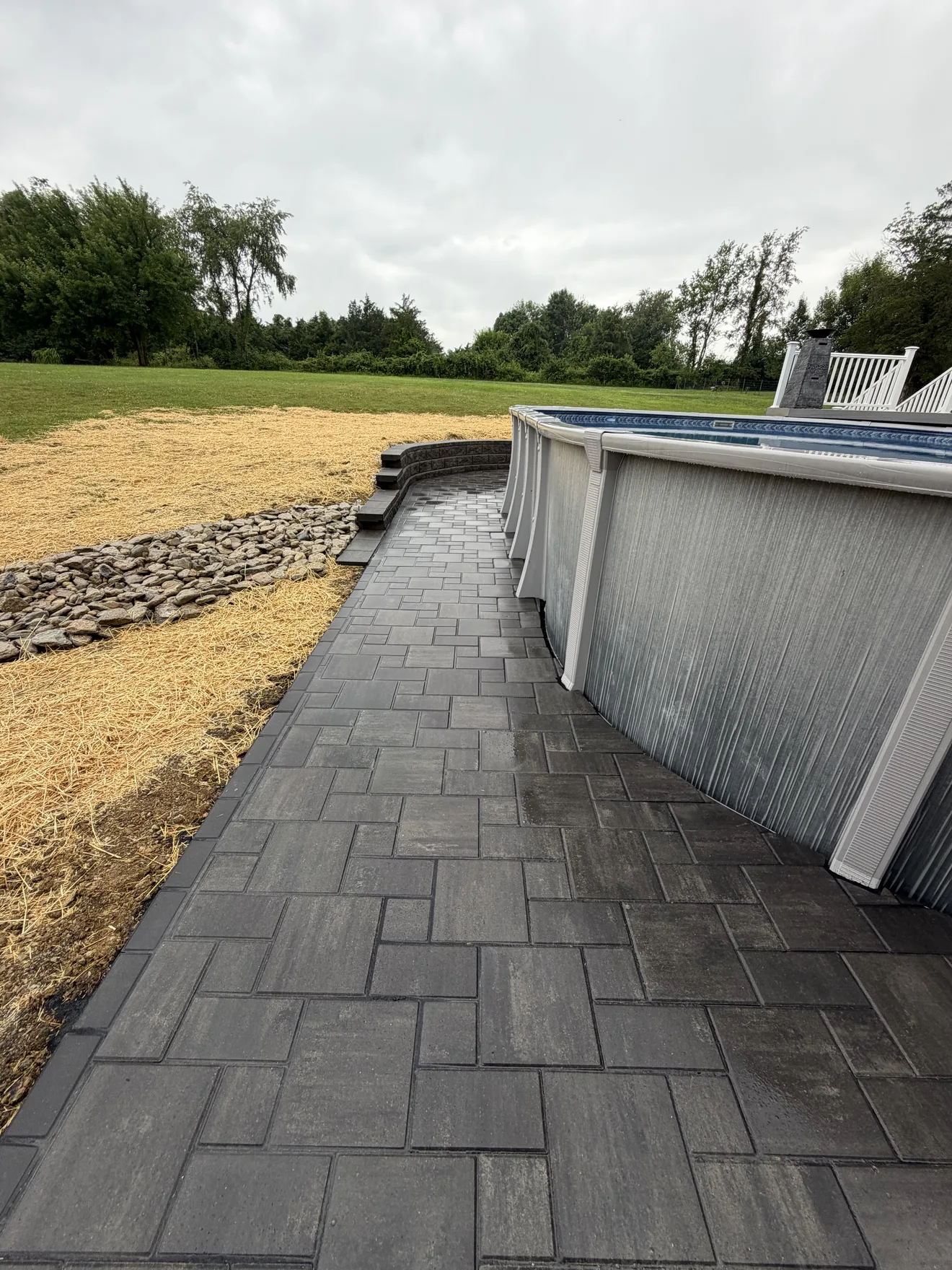 Gray paver patio with a charcoal border wrapping the pool in Lebanon, OH, rock rainscape alongside