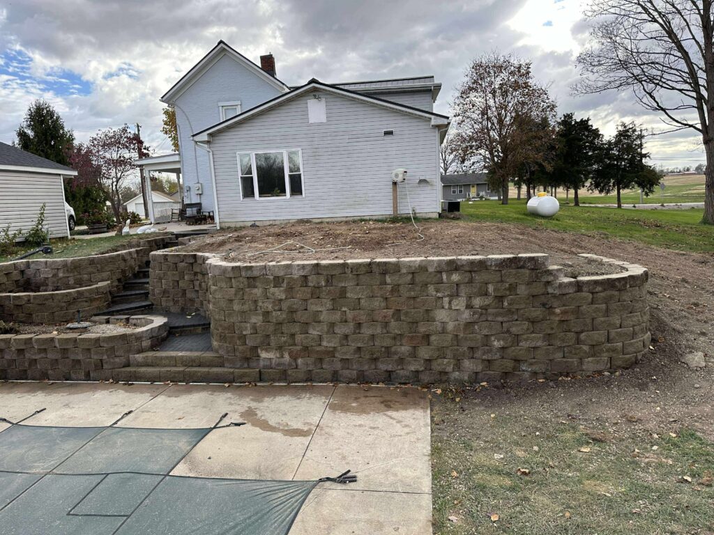Massive retaining wall with curved steps constructed using geogrid reinforcement and over 50 tons of gravel backfill by Shawn’s Landscape & Design in Gratis, Ohio to correct drainage issues