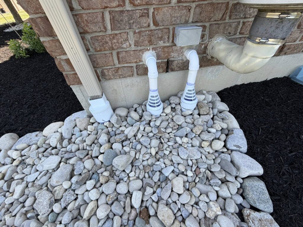 After downspout drainage correction with clean drainage outlets, river rock, black mulch, and improved water flow away from the foundation.